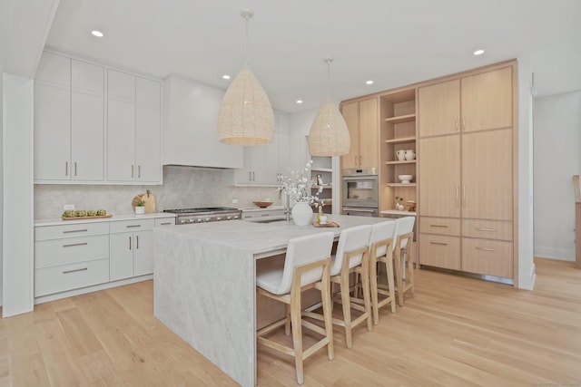 kitchen featuring white cabinets, decorative light fixtures, light hardwood / wood-style floors, and an island with sink