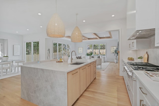 kitchen featuring white cabinets, an island with sink, wall chimney exhaust hood, and sink