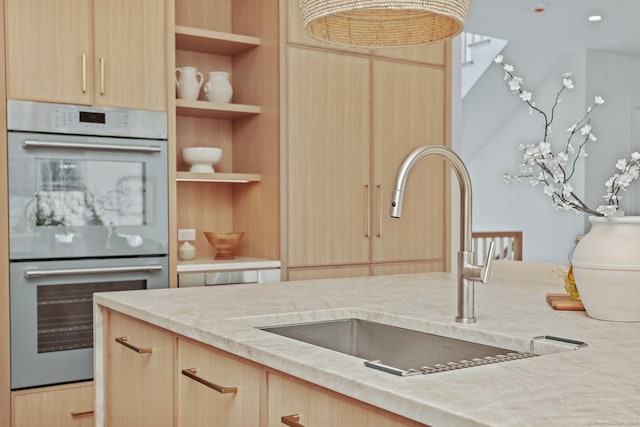 kitchen featuring light stone counters, built in shelves, double oven, sink, and light brown cabinets