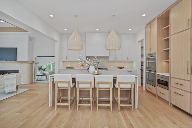 kitchen with built in microwave, hanging light fixtures, backsplash, an island with sink, and white cabinets