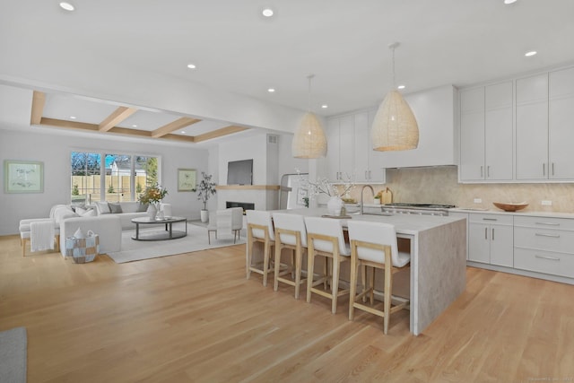 kitchen with an island with sink, light hardwood / wood-style floors, a breakfast bar area, white cabinets, and custom range hood