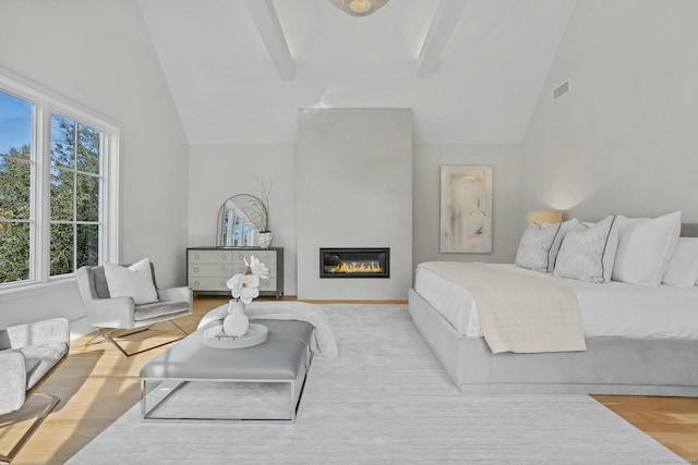 bedroom with lofted ceiling with beams, light wood-type flooring, and a fireplace