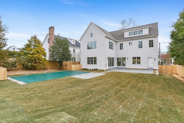 rear view of property with a covered pool, a patio area, and a lawn