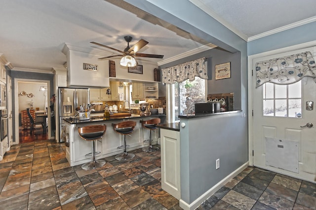 kitchen featuring kitchen peninsula, a kitchen bar, stainless steel appliances, ceiling fan, and crown molding