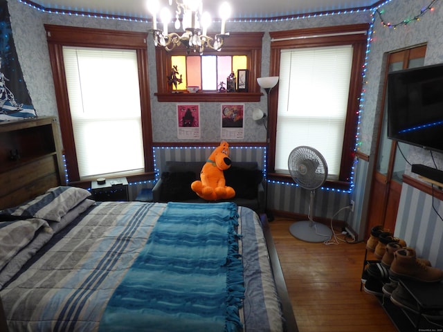 bedroom featuring radiator, multiple windows, hardwood / wood-style floors, and a notable chandelier