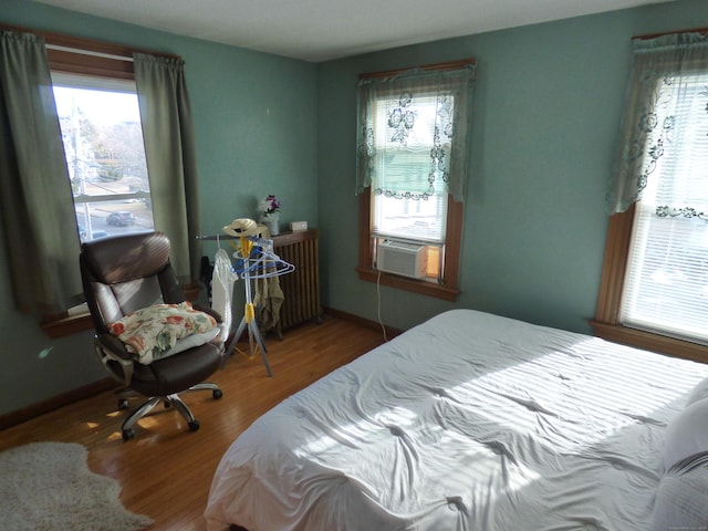 bedroom featuring hardwood / wood-style floors, radiator heating unit, and multiple windows