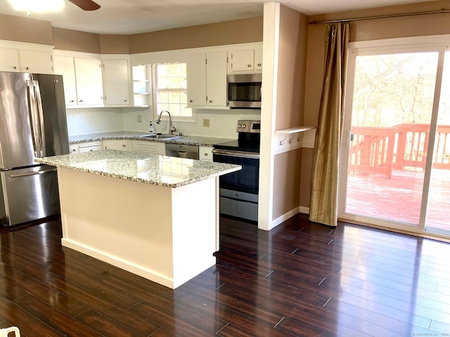 kitchen with light stone countertops, stainless steel appliances, sink, white cabinets, and a center island