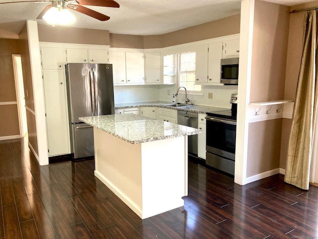 kitchen featuring light stone countertops, stainless steel appliances, sink, a center island, and white cabinetry