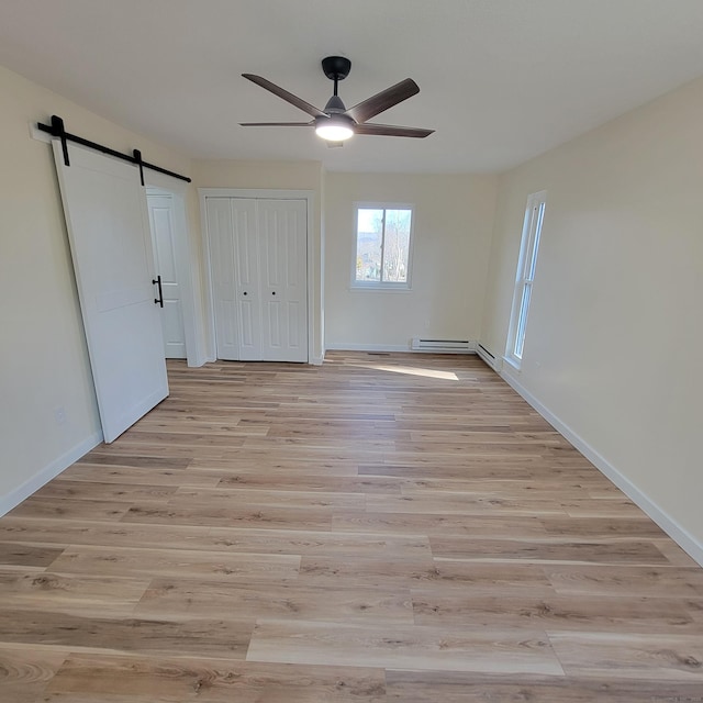 unfurnished bedroom featuring light wood-type flooring, ceiling fan, a barn door, and a baseboard heating unit