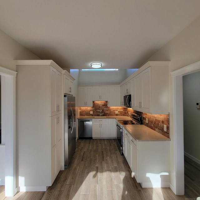 kitchen with hardwood / wood-style floors, white cabinets, appliances with stainless steel finishes, sink, and backsplash