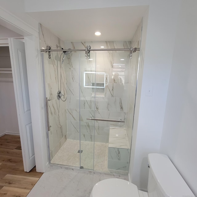 bathroom with a shower with shower door, hardwood / wood-style floors, and toilet