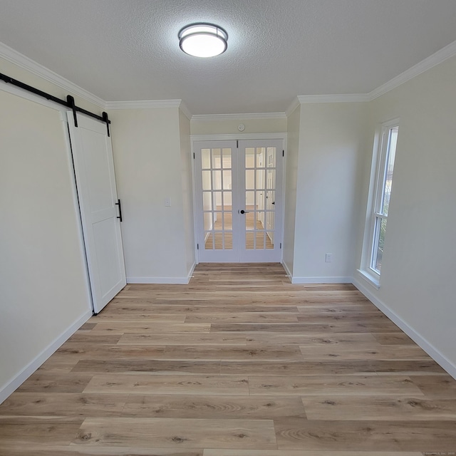 spare room featuring french doors, light hardwood / wood-style flooring, ornamental molding, and a barn door