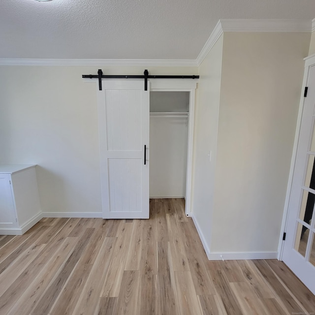 unfurnished bedroom with a textured ceiling, a closet, ornamental molding, light hardwood / wood-style flooring, and a barn door