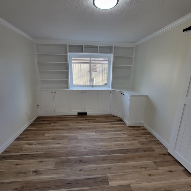 spare room featuring a textured ceiling, ornamental molding, built in features, and light hardwood / wood-style flooring