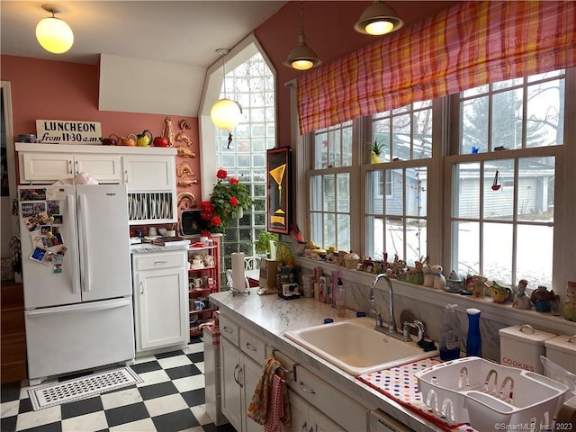 kitchen with hanging light fixtures, sink, white refrigerator, white cabinets, and plenty of natural light