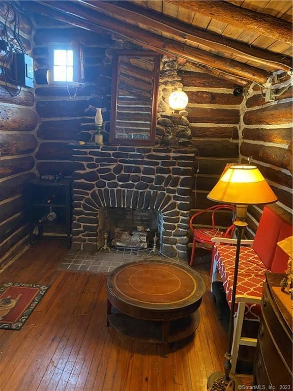 sitting room with rustic walls, lofted ceiling with beams, wood-type flooring, a fireplace, and wood ceiling