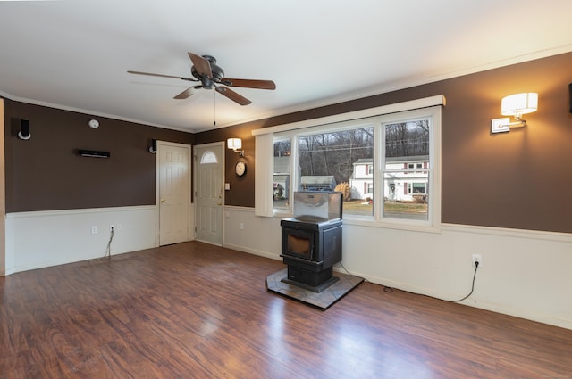 unfurnished living room with hardwood / wood-style floors, a wood stove, ceiling fan, and crown molding