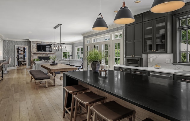 kitchen with a stone fireplace, light hardwood / wood-style flooring, crown molding, decorative light fixtures, and a kitchen bar