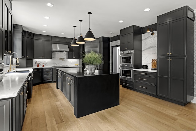 kitchen with backsplash, stainless steel double oven, wall chimney range hood, pendant lighting, and a center island