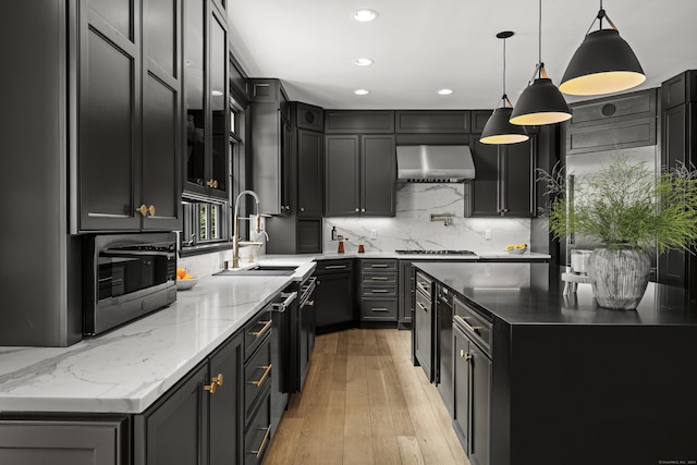 kitchen with sink, hanging light fixtures, wall chimney range hood, backsplash, and light hardwood / wood-style floors