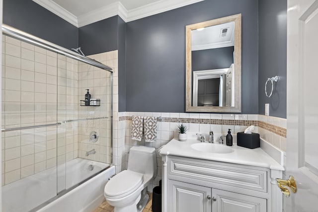 full bathroom featuring vanity, shower / bath combination with glass door, crown molding, toilet, and tile walls