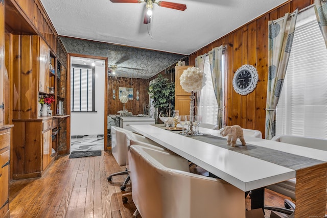 dining space featuring a textured ceiling, light hardwood / wood-style flooring, ornamental molding, and wood walls