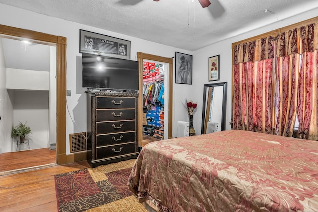 bedroom with radiator, ceiling fan, a textured ceiling, wood-type flooring, and a closet