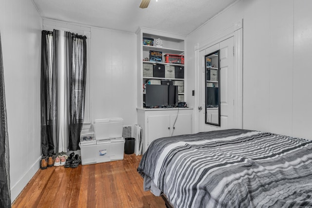 bedroom featuring ceiling fan, wood walls, wood-type flooring, and a textured ceiling