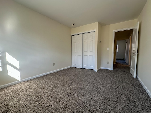 unfurnished bedroom with baseboard heating, a closet, and dark carpet