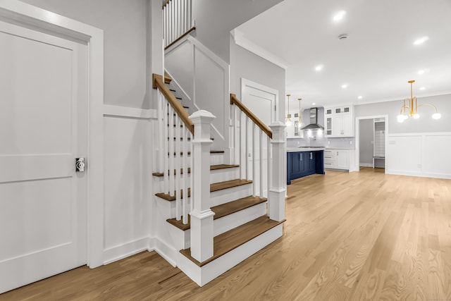 stairway with ornamental molding, recessed lighting, wood finished floors, and a notable chandelier