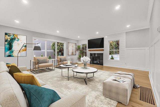 living room with recessed lighting, light wood-type flooring, a fireplace, and crown molding