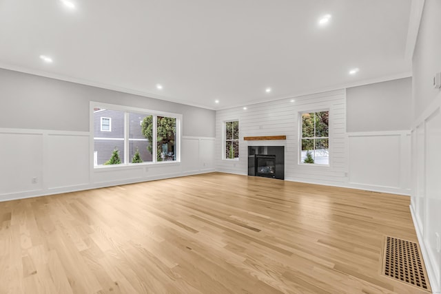 unfurnished living room featuring light wood finished floors, a glass covered fireplace, visible vents, and a healthy amount of sunlight