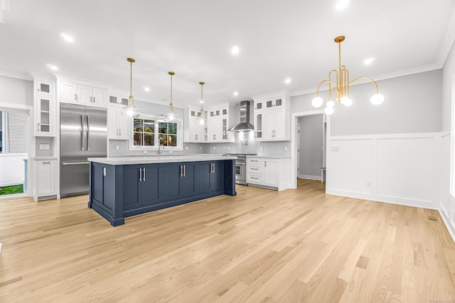 kitchen with wall chimney exhaust hood, white cabinetry, light countertops, and premium appliances