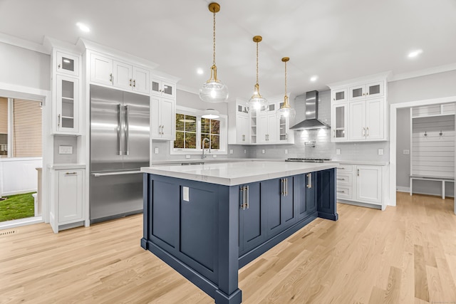 kitchen with blue cabinets, stainless steel built in fridge, white cabinets, a center island, and wall chimney exhaust hood