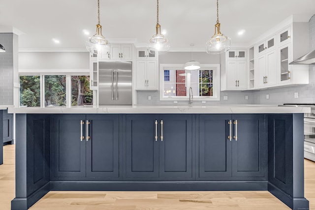 kitchen featuring wall chimney range hood, backsplash, stainless steel built in refrigerator, and light countertops