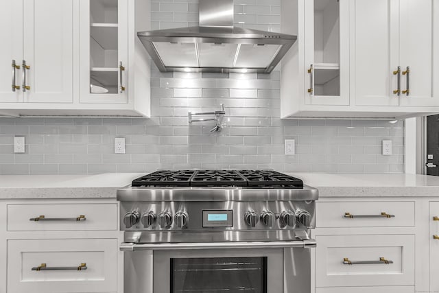 kitchen featuring exhaust hood, white cabinetry, high end stainless steel range oven, tasteful backsplash, and glass insert cabinets