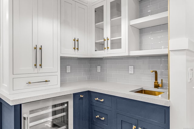 kitchen with blue cabinetry, tasteful backsplash, white cabinetry, a sink, and beverage cooler