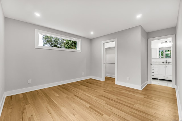 unfurnished bedroom with multiple windows, light wood-type flooring, a sink, and baseboards