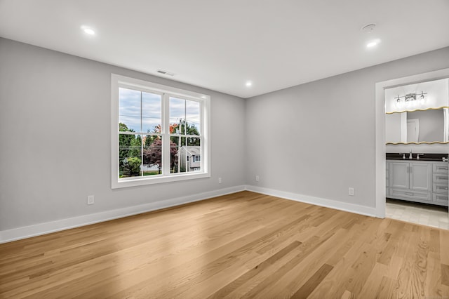 spare room with light wood finished floors, visible vents, baseboards, a sink, and recessed lighting