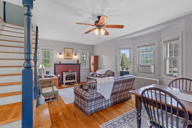 living room with a textured ceiling, ceiling fan, cooling unit, light hardwood / wood-style flooring, and a wood stove