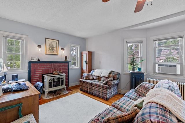 living room with a wood stove, ceiling fan, cooling unit, a textured ceiling, and light wood-type flooring