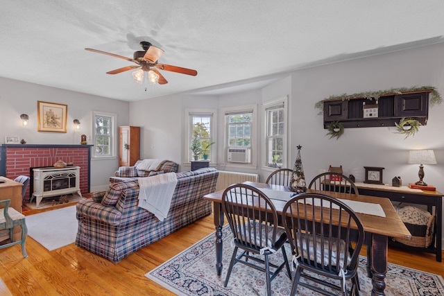 dining space with a wood stove, ceiling fan, cooling unit, a textured ceiling, and light wood-type flooring