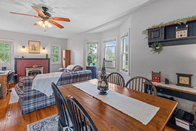 dining space with ceiling fan, wood-type flooring, a wood stove, and plenty of natural light