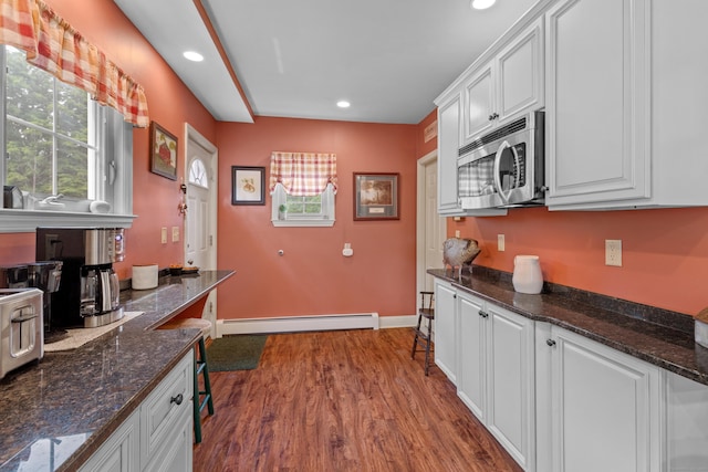 kitchen with dark stone countertops, white cabinetry, light hardwood / wood-style flooring, and a baseboard heating unit