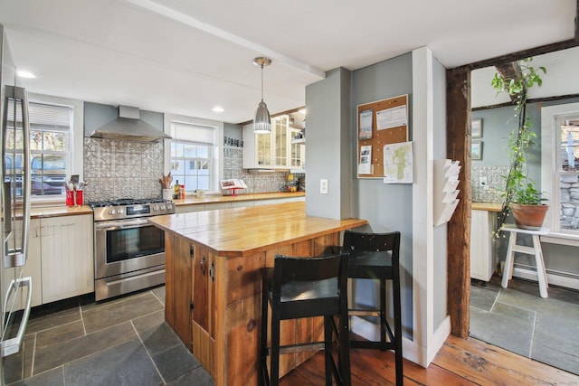 kitchen featuring a breakfast bar, decorative backsplash, hanging light fixtures, stainless steel appliances, and wall chimney exhaust hood