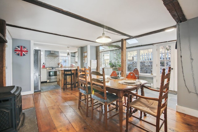 dining space with beamed ceiling, wood-type flooring, and a wood stove