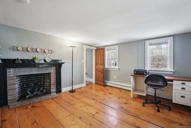 office space featuring a baseboard radiator, a brick fireplace, and light wood-type flooring