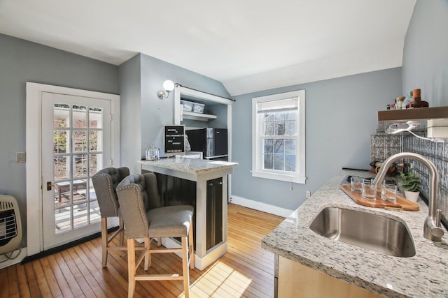 kitchen featuring lofted ceiling, sink, heating unit, light stone counters, and light hardwood / wood-style floors