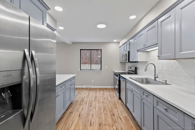 kitchen featuring decorative backsplash, light stone counters, stainless steel appliances, sink, and light hardwood / wood-style floors