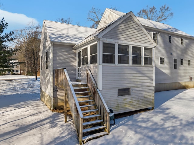 snow covered back of property featuring a sunroom